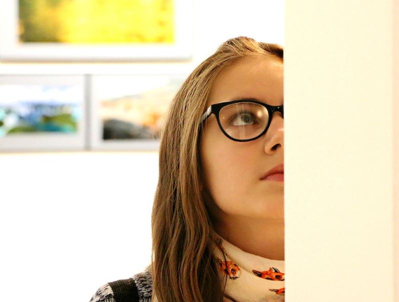 a girl with eyeglasses, three paintings behind the girl